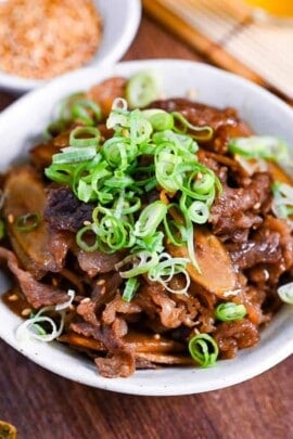 Beef shigureni with ginger and burdock root in a white dish topped with chopped green onion