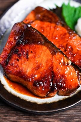 Japanese buri no teriyaki (yellowtail teriyaki) on a brown rimmed plate decorated with a perilla leaf and grated daikon radish