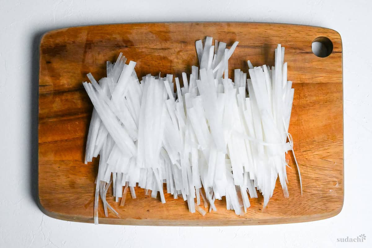 Daikon radish cut into matchsticks on a wooden chopping board