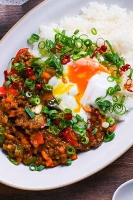 Japanese dry curry on a white oval plate topped with green onions, red chilis and onsen tamago top down