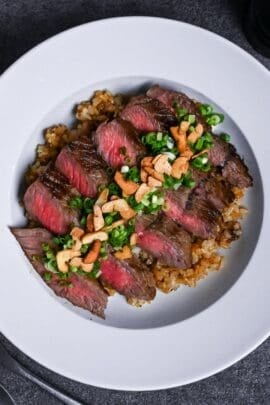 garlic fried rice topped with rare pan-fried beef steak slices, chopped green onions and crispy garlic chips in a white dish thumbnail