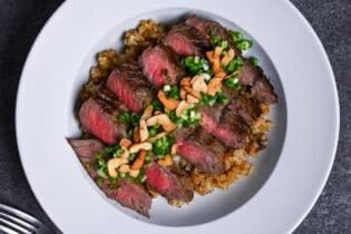 garlic fried rice topped with rare pan-fried beef steak slices, chopped green onions and crispy garlic chips in a white dish thumbnail