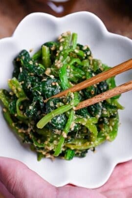 Japanese Sesame Spinach Salad (Horenso Goma Ae) in a white bowl in a hand with wooden chopsticks