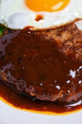 Japanese hamburg steak (hambagu) coated with homemade sauce on a white plate served with rice, vegetables and a fried egg thumbnail