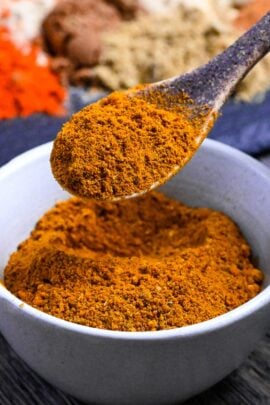 Homemade Japanese curry powder in a small white bowl heaped on a brown ceramic spoon