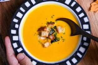 Japanese style kabocha soup topped with homemade croutons and kabocha skin in a white bowl with blue patterned rim