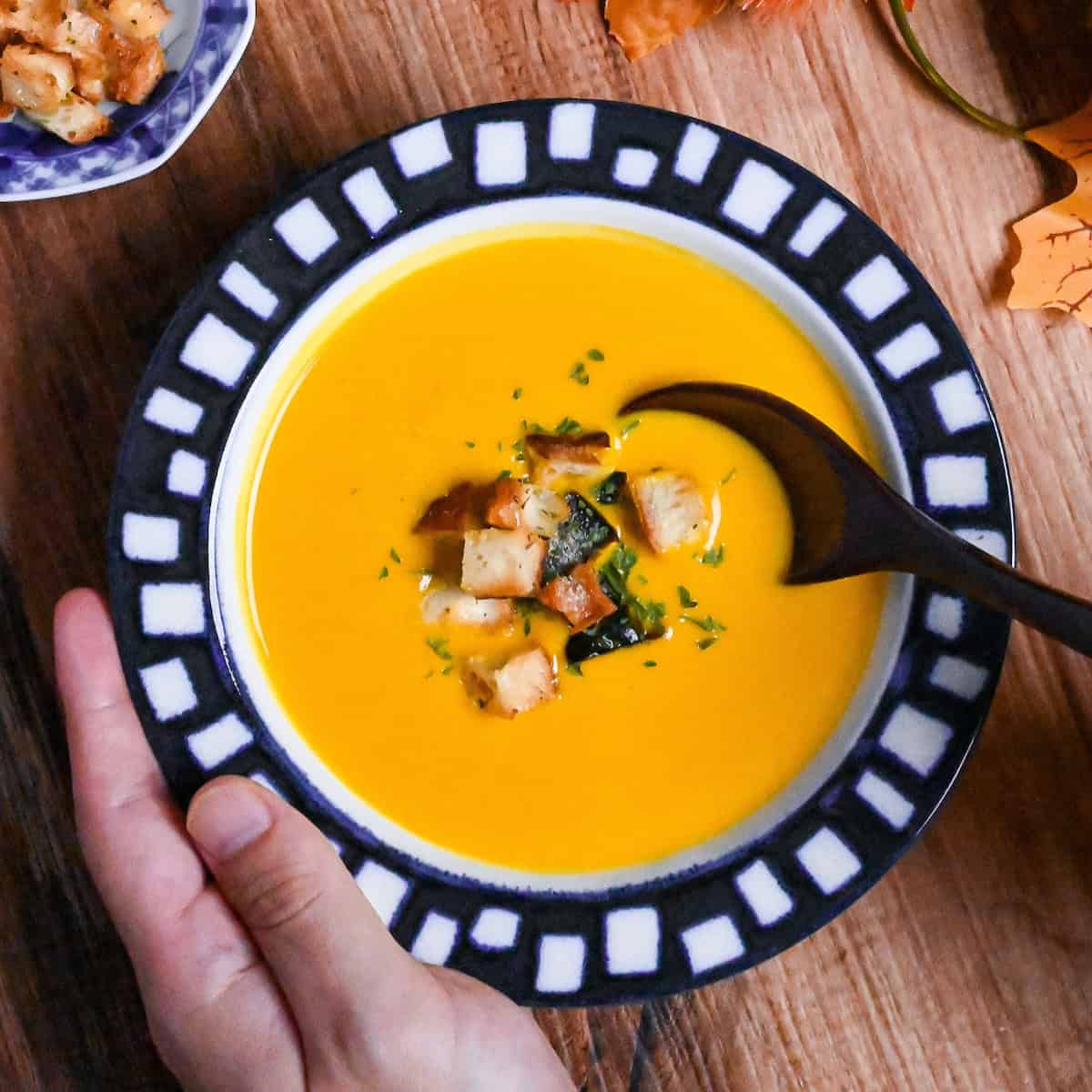 Japanese style kabocha soup topped with homemade croutons and kabocha skin in a white bowl with blue patterned rim
