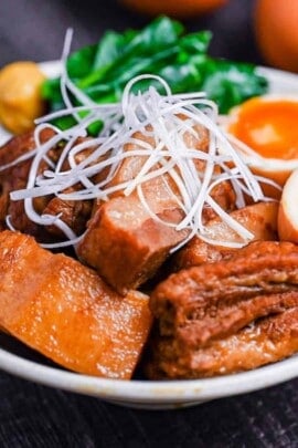 Buta no kakuni (Japanese braised pork belly) in an off-white dish with marinated soft boiled eggs, mustard spinach and a blob of mustard topped with shredded green onion