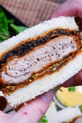 two hands holding up a Japanese pork cutlet sandwich with red miso sauce (miso katsu sando)