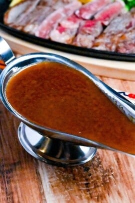 Japanese steakhouse style steak sauce in a steel gravy boat with slices of rare beef in the background