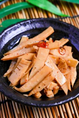 Menma-style seasoned bamboo shoots ramen topping in a black bowl on a bamboo background