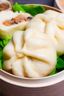 Japanese "nikuman" steamed pork buns in a bamboo steamer arranged over green frilly lettuce