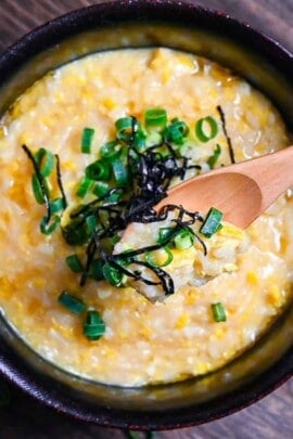 Okayu (Japanese Rice Porridge) with egg in a black lacquerware bowl sprinkled with spring onion and kizami nori