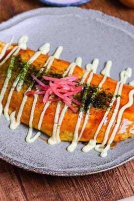 omusoba on a beige plate drizzled with okonomi sauce, Japanese mayo and topped with aonori and red pickled ginger