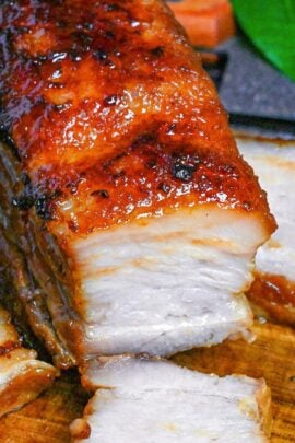A block of Japanese chashu-style oven baked pork belly for ramen on a wooden chopping board with a few slices scattered around