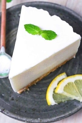 A slice of lemon rare cheesecake topped with a mint leaf and served on a dark green plate