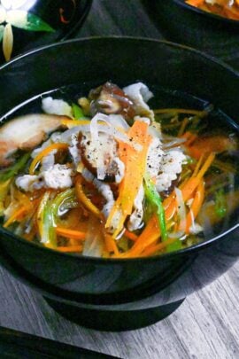 Sawaniwan (Japanese pork and vegetable soup) in a black bowl on a ashy wood background