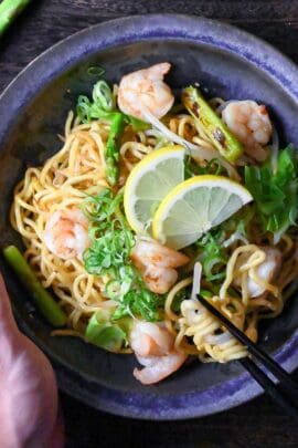 Shio Lemon Yakisoba in a blue/black iridescent bowl held with a hand and black chopsticks lifting noodles top down view