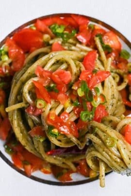 Japanese shiso pesto pasta topped with marinated tomato in a white pasta dish with silver fork top down
