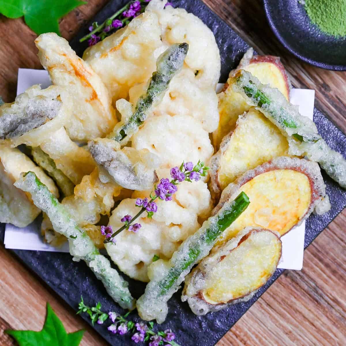 Eggless Vegetable Tempura (shojin-age) with homemade matcha salt served on a square black plate decorated with purple flowers