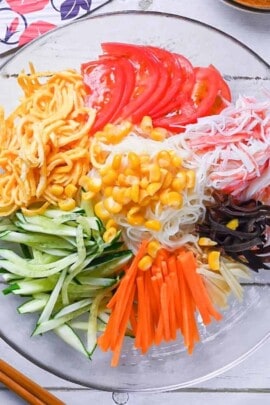 Somen salad served in a glass dish with imitation crab, kinshi tamago, tomatoes, cucumber, carrot, woodear mushrooms and sweetcorn served with thick and creamy wasabi and sesame dressing.