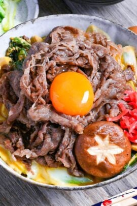 Sukiyaki beef donburi rice bowl topped with red pickled ginger, shiitake mushroom and egg yolk in a mottled bowl featured image