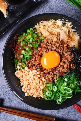 Taiwan Mazesoba served in a black ramen bowl and topped with seasoned pork mince, spring onions, Chinese chives, katsuobushi, tenkasu, kizami nori and a raw egg yolk