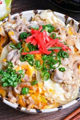 Tanin Don (Japanese pork and egg rice bowl) in a striped bowl topped with red pickled ginger and chopped green onions