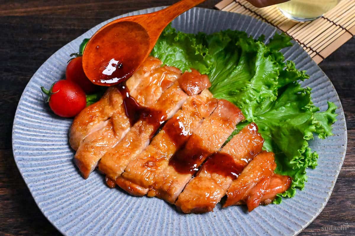 A wooden spoon drizzling teriyaki chicken with leftover sauce