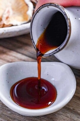 pouring homemade tsuyu sauce into dipping dish next to a plate of shiitake, kombu and bonito flakes (dashi ingredients)