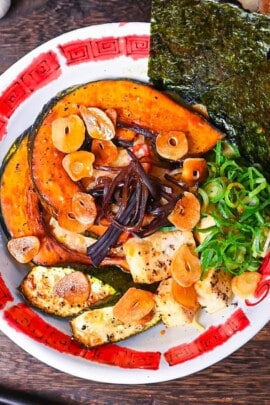Spicy vegetarian miso ramen topped with oven baked kabocha, tofu and zucchini in a red and white bowl