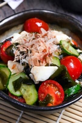 Japanese wakame salad made with wakame seaweed, mini tomatoes, cucumber and silken tofu served in a mottled gray bowl with dark brown edge