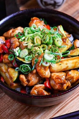 Yakitori donburi made with chicken, zucchini, green onions and bell peppers cooked in a yakitori-style tare (sauce) served in a black bowl and topped with green onion and shichimi