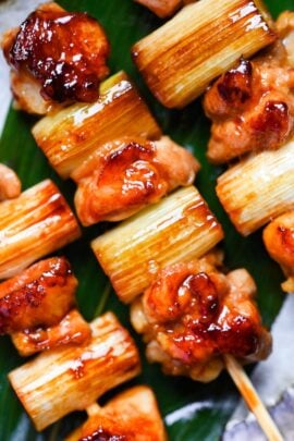 three negima yakitori Japanese chicken skewers on an oval plate with decorative leaf