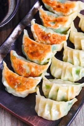 prawn gyoza arranged in rows on a brown rectangular plate with dipping sauce