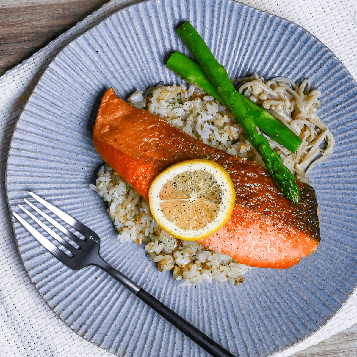 Butter Soy Sauce Salmon (Japanese-Style Salmon Meunière) on a bed of garlic rice next to sautéed asparagus and enoki mushrooms on a blue striped dinner plate top down