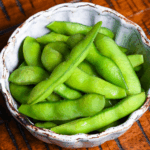 Izakaya style salt boiled edamame in an off-blue bowl on a wooden table with black lines
