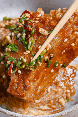 Close up of sauce coated crispy enoki mushrooms held up with wooden chopsticks