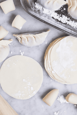 homemade gyoza wrappers in a stack next to a tray of homemade gyoza