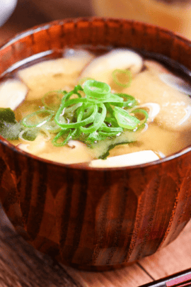 homemade Japanese miso soup in a dark wooden soup bowl with red and black chopsticks