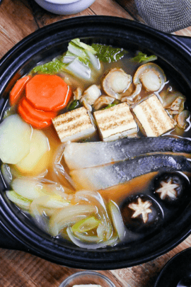 Hokkaido Style Ishikari Nabe (Salmon and Miso Hot Pot) with vegetables, tofu and scallops in a black Japanese "nabe" pot on a wooden background top down