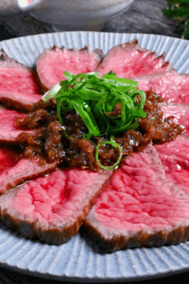 Japanese style roast beef cooked rare, cut into thin slices and topped with a wafu sauce and chopped green onions on a blue plate