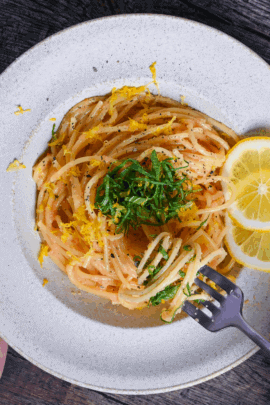Mentaiko Pasta topped with shredded perilla leaves and lemon zest with a hand holding a fork with some pasta twirls around it