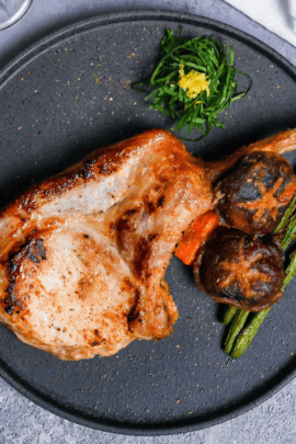 Miso marinated pork chop and roasted vegetables on a dark gray plate with shredded shiso leaves and yuzu peel