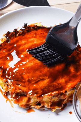 Homemade okonomiyaki sauce being brushed onto a freshly cooked okonomiyaki