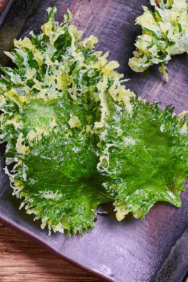 Three ooba (shiso) tempura made with Perilla leaves on a brown/purple plate on a wooden background