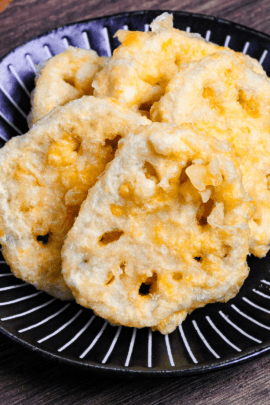 Five pieces of renkon tempura (lotus root) on a black plate with white stripes on a dark wooden background