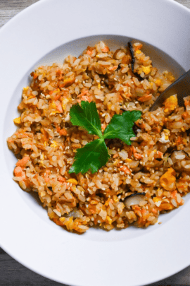 Salmon fried rice served in a white dish and garnished with mitsuba (Japanese wild parsley) with silver spoon