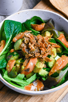 crispy salmon skin salad in a white bowl on a wooden chopping board with a wooden spoon in the background