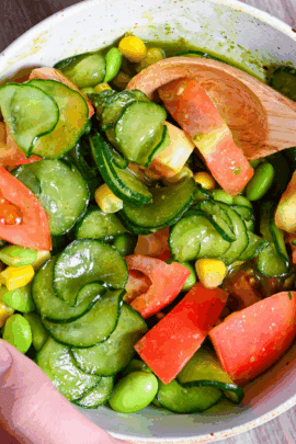 a hand holding a bowl filled with summer vegetable salad and shiso dressing with a wooden spoon close up
